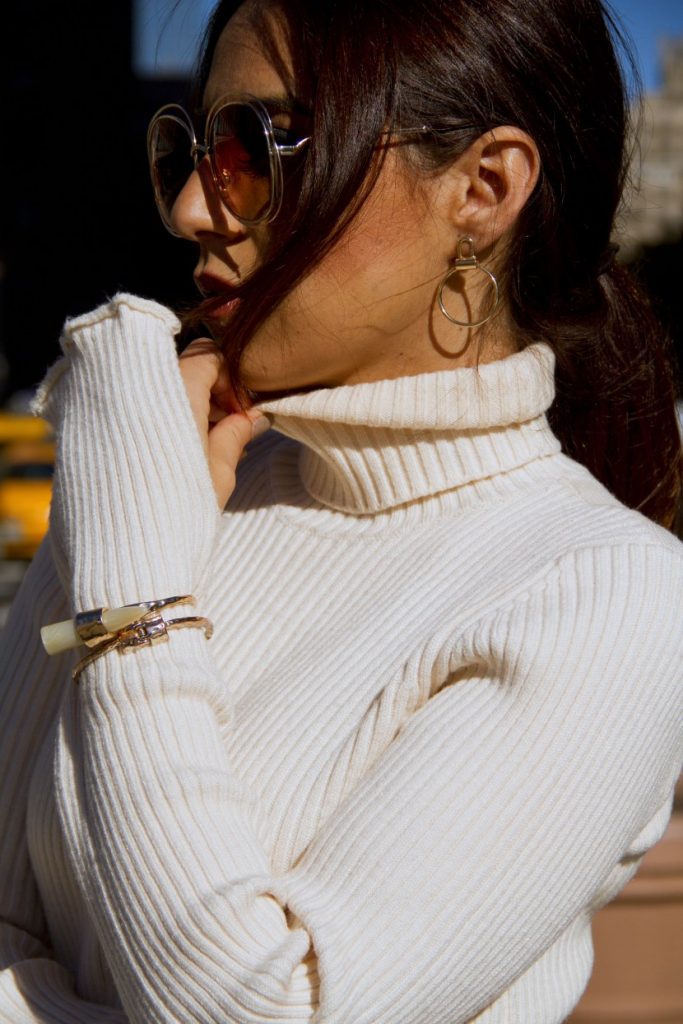 NEW YORK, NY - NOVEMBER 10: Ana Sousa wearing Ecru white ribbed knit sweater with polo neck and long sleeves with slit from Zara, gold and pearl bangle bracelets by Zara, Ralph Lauren gold round orbital drop earrings and rose gold carlina oversized round metal sunglasses by Chloe on November 10, 2016 in New York City. (Photo by Georgie Hunter/Getty Images)